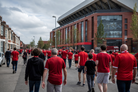 Crowds in red approaching Anfield stadium on a bright match-day afternoon