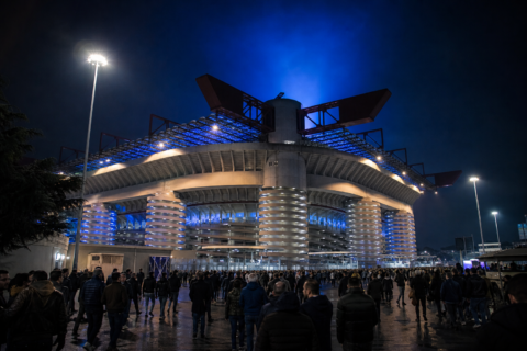 Floodlit San Siro on a European night with fans streaming toward the gates