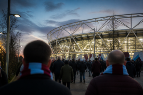 West Ham fans in claret and blue walking toward London Stadium at dusk