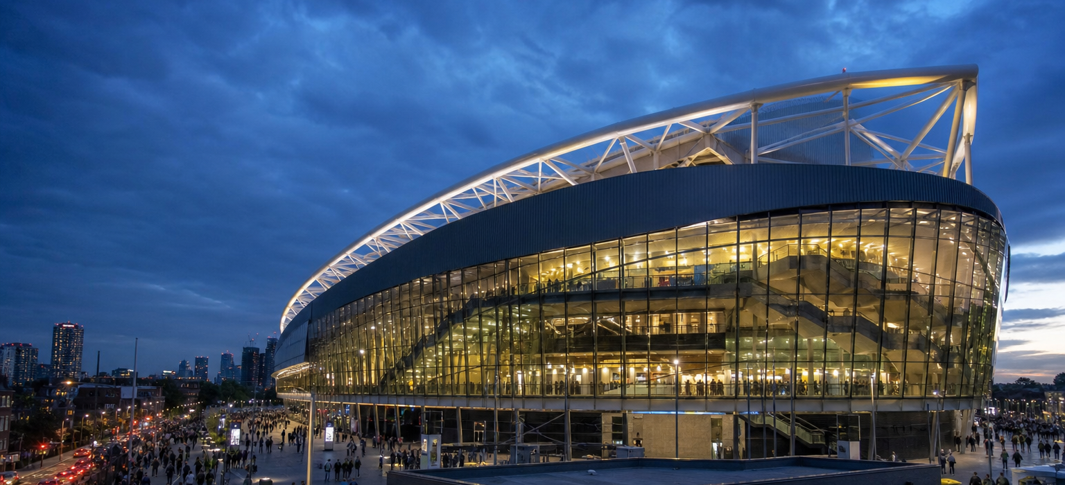 Tottenham Hotspur Stadium exterior glowing at dusk with crowds on the concourse