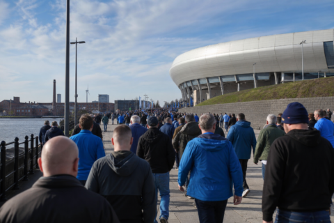 Everton supporters in blue walking toward a Merseyside stadium on match day
